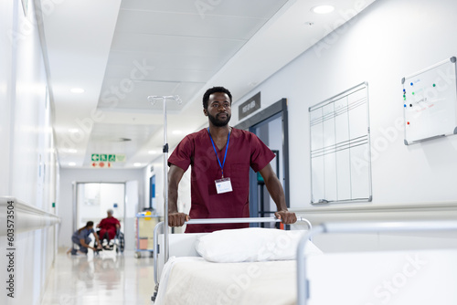 African american male medical worker pushing empty bed in hospital corridor
