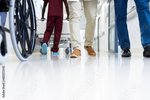 Low section of diverse male doctors and wheelchair in busy hospital corridor, copy space