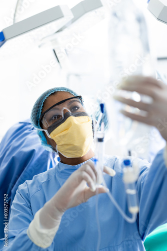 African american female surgeon with face mask preparing drip in operating room