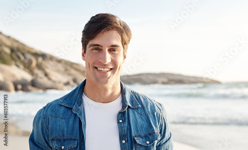 Man, portrait and beach with sunshine and smile in the outdoors for an adventure and happiness. Ocean, sun and male person is happy in the outdoor for day to relax in the summer with nature and air.