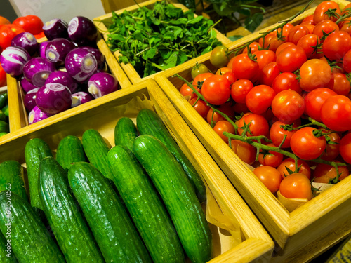 beautiful washed cucumbers and tomatoes lie neatly in a wooden box next to boxes with other vegetables. shop, restaurant, market, home