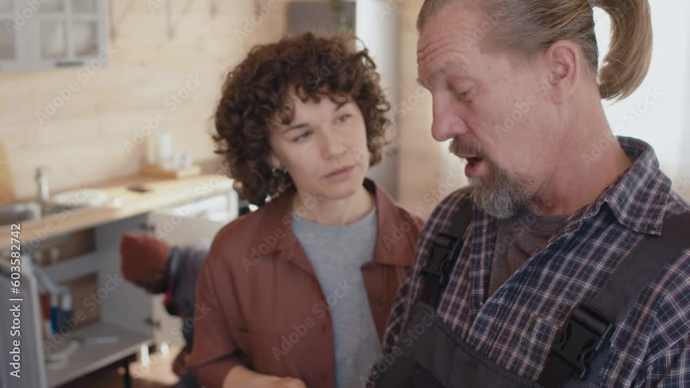 Selective focus of modern repairman holding digital tablet and female client standing in kitchen discussing work Selective focus of modern repairman holding digital tablet and female client standing in kitchen discussing work
