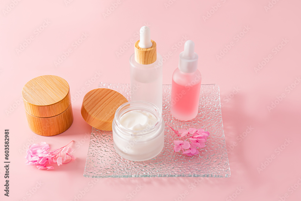 A fashionable cosmetic product in glass matte white bottles and cream in a jar on a glass embossed tray and a pink background. natural cosmetics.