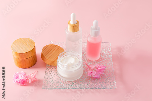 A fashionable cosmetic product in glass matte white bottles and cream in a jar on a glass embossed tray and a pink background. natural cosmetics.