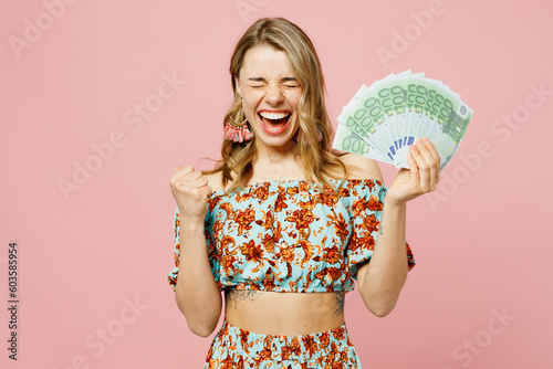 Young blonde woman wears summer casual clothes hold in hand fan of cash money in dollar banknotes do winner gesture isolated on plain pastel light pink background studio portrait. Lifestyle concept.