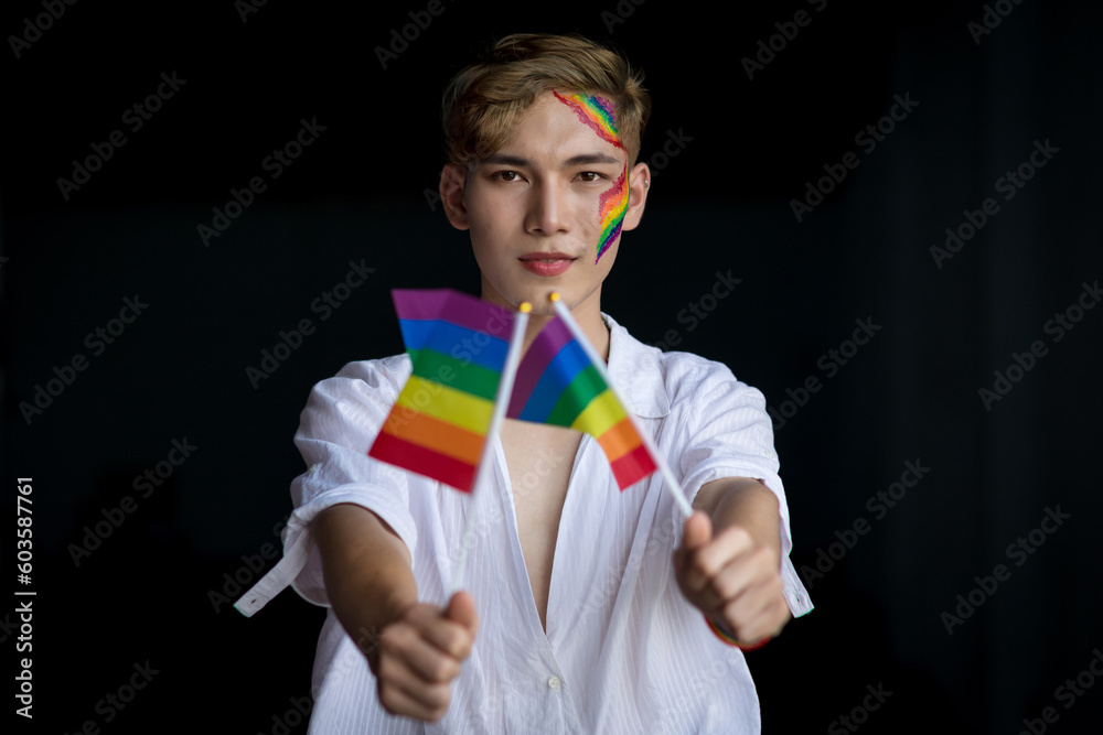 Handsome Asian gay man with pride LGBT rainbow flag on black background ...