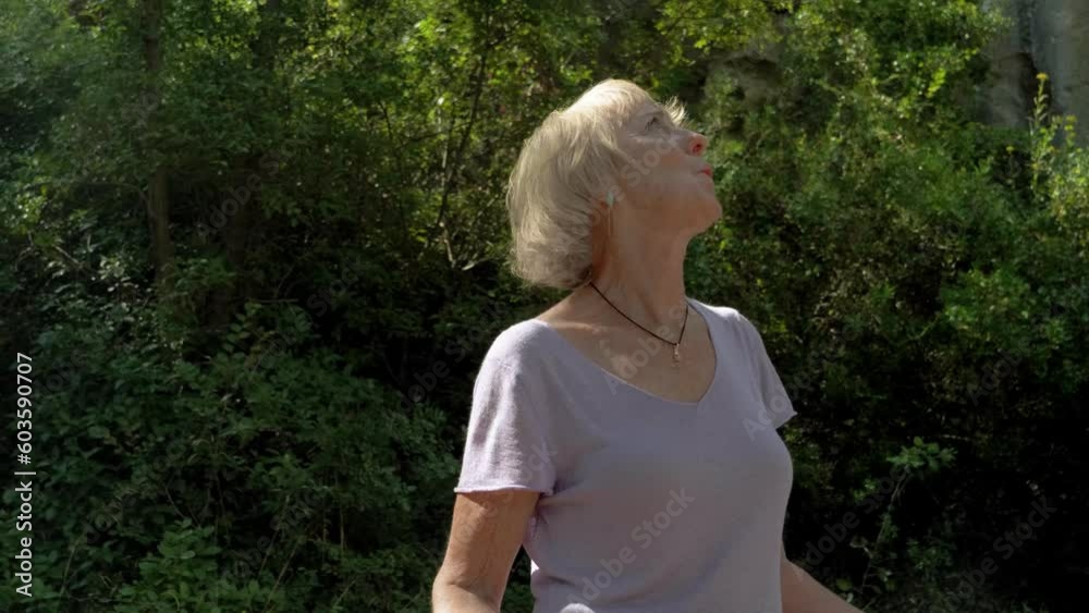 Orbit shot of old lady connecting with the forest spiritually and smiling