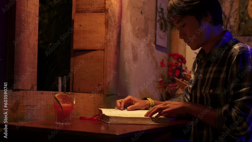 Close up of young asian man studying from book with a juice on table at night time Close up of young asian man studying from book with a juice on table at night time