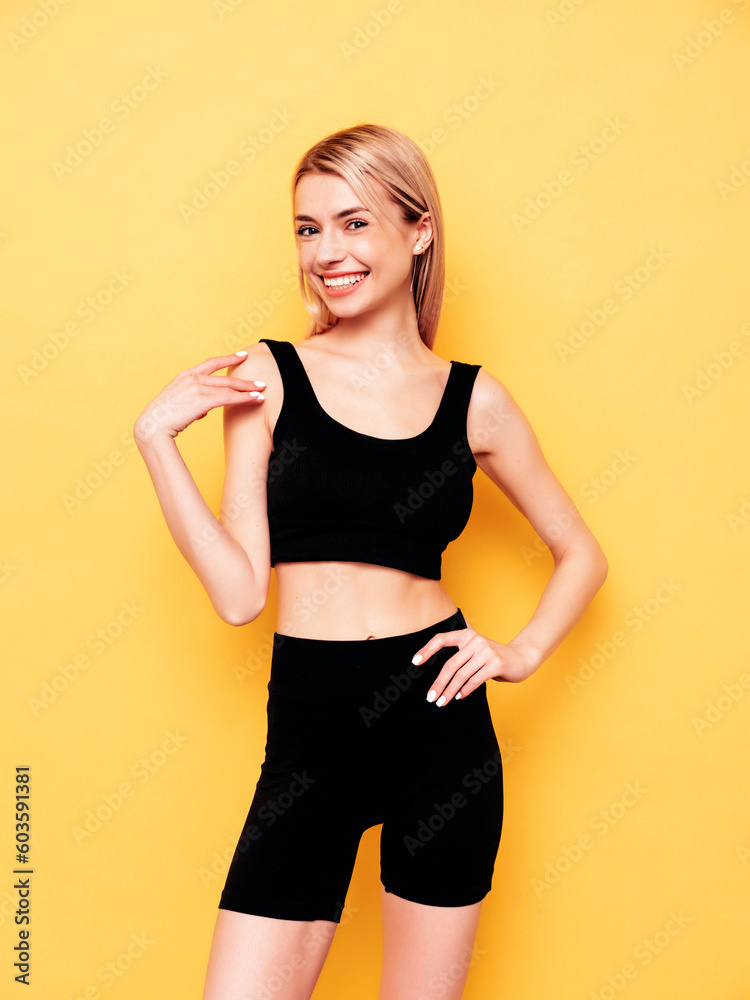 Young beautiful smiling blond female in summer black cycling shorts clothes. Sexy carefree woman posing near yellow wall in studio. Positive model having fun indoors. Cheerful and happy Young beautiful smiling blond female in summer black cycling shorts clothes. Sexy carefree woman posing near yellow wall in studio. Positive model having fun indoors. Cheerful and happy