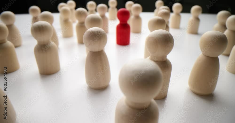 Lonely red figure surrounded by white wooden figurines standing on table surface. Leadership with nonconformity and different opinion concept