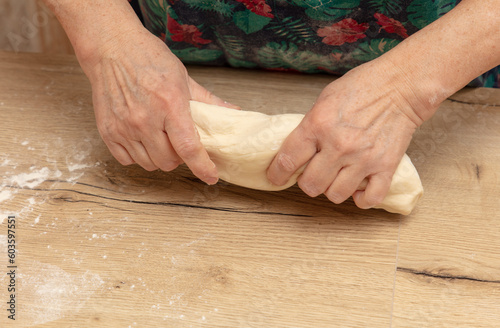 Elderly woman kneading dough on a wooden table in the kitchen