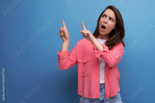 shocked black haired lady in casual style pointing finger at wall in studio background