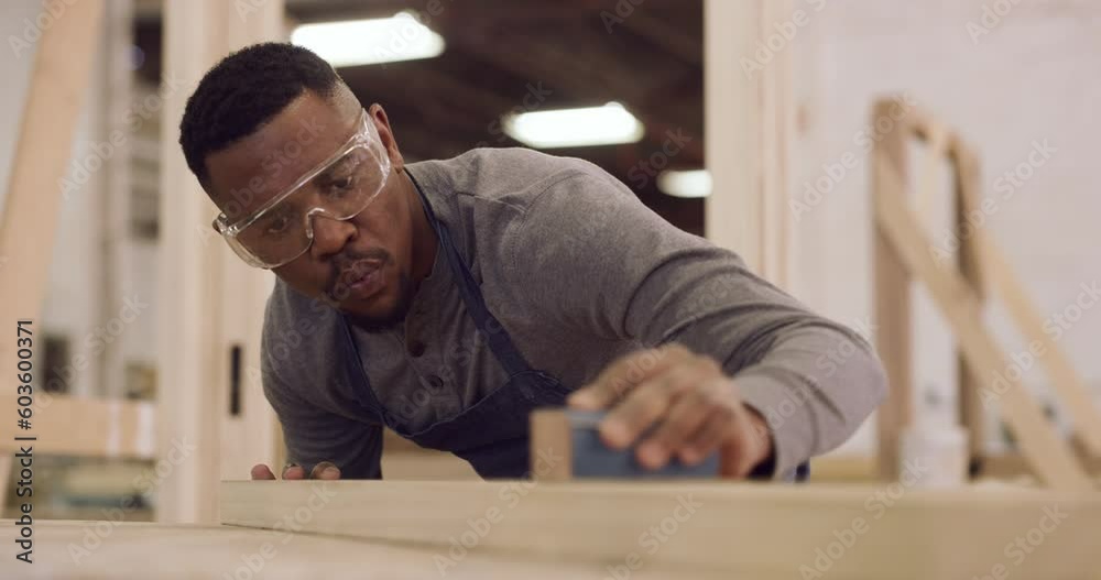 Carpentry, design and sandpaper with a black man in his factory to finish a professional woodwork project. Safety goggles, manual labor and expertise with a carpenter sanding in his creative workshop