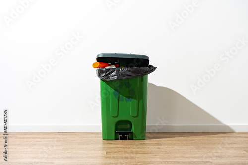 Green plastic trash can full of garbage indoors