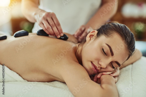 Spa, zen and woman getting a hot stone back massage for luxury, calm and natural self care. Beauty, body care and tranquil female person sleeping while doing a rock body therapy treatment at a salon.