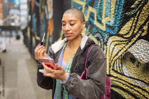 Hipster young woman applying lip gloss in street photo