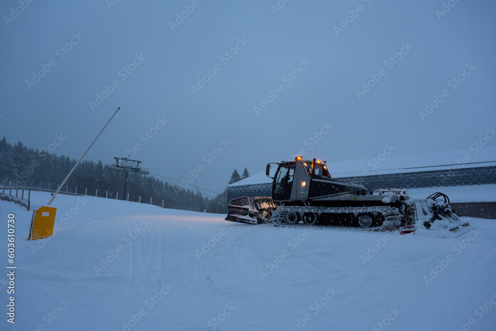 Snow groomer on ski slope at night