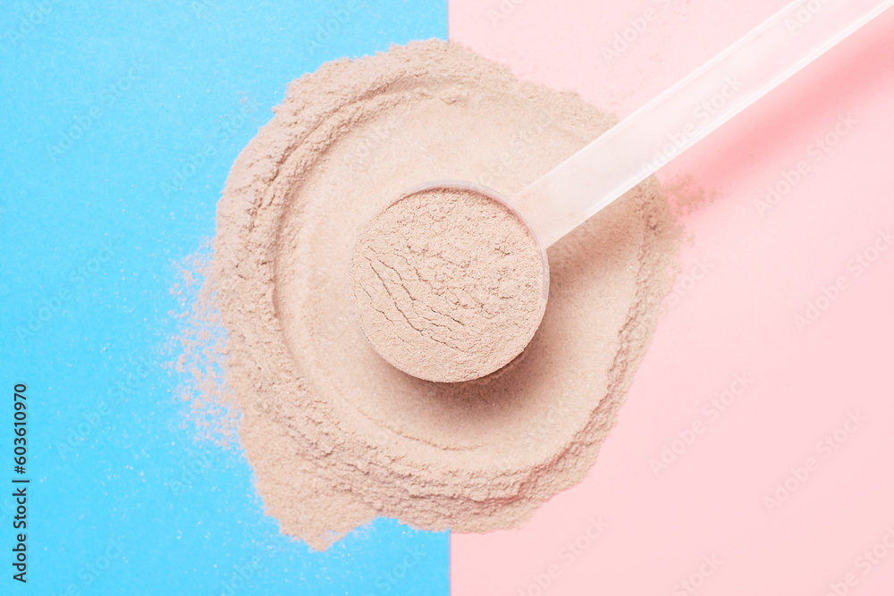 Scattered protein and measuring spoon on blue and pink background top view, concert of sports nutrition. Scattered protein and measuring spoon on blue and pink background top view, concert of sports nutrition.