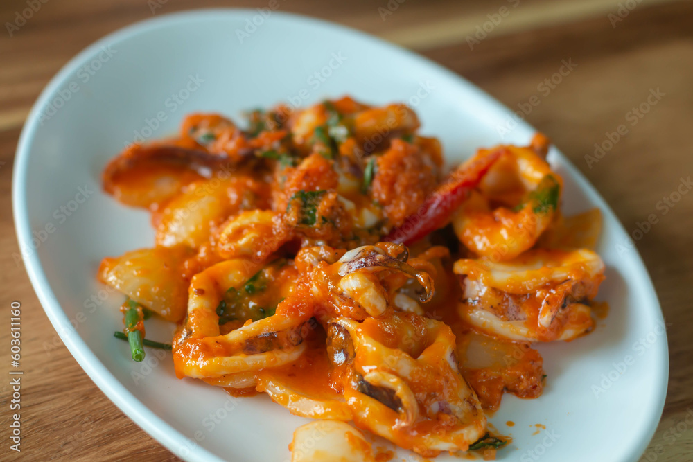 Stir fried squid with salted egg yolk on white dish on table background, closeup Stir fried squid with salted egg yolk on white dish on table background, closeup