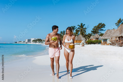 Hispanic young couple holding a coconut and having fun on caribbean beach in holidays or vacations in Mexico Latin America photo