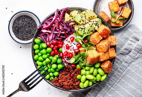 Healthy vegan food. Buddha bowl with quinoa, fried tofu, avocado, edamame, green peas, radish, cabbage and sesame seeds. White kitchen table background, top view