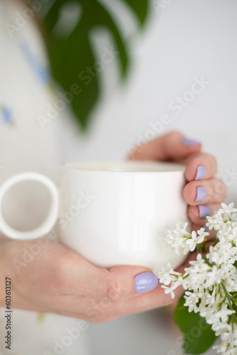 A cup of morning coffee in female hands and flowers on a white background