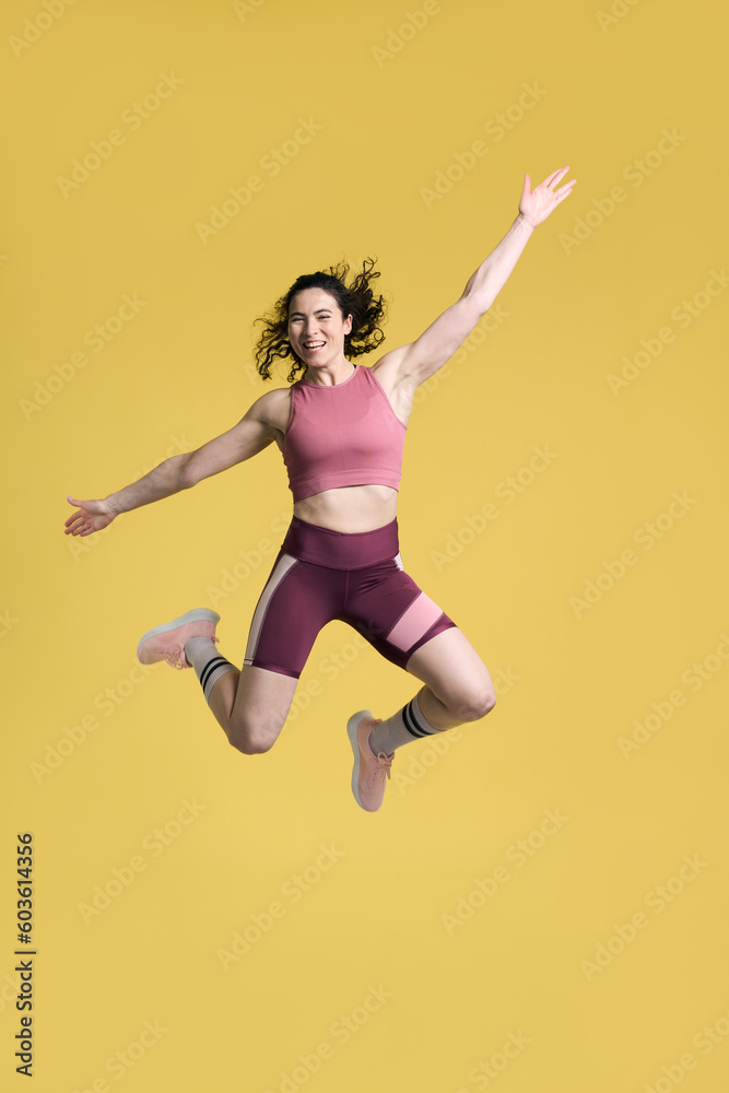 Full length portrait smiling athletic woman, jumping high up over yellow isolated background. Sport