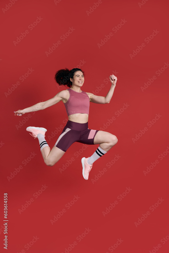 Determined young Caucasian sportswoman jumping high up, succeed training on isolated red background