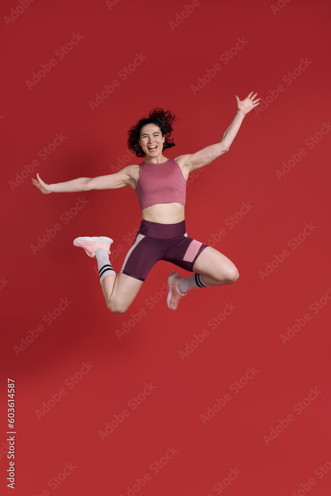 Full length studio portrait of female athlete jumping over red background. Sport Fitness Workout