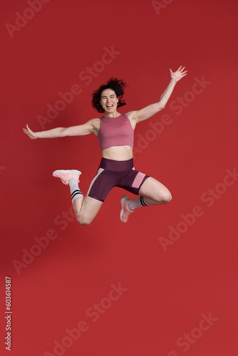 Full length studio portrait of female athlete jumping over red background. Sport Fitness Workout