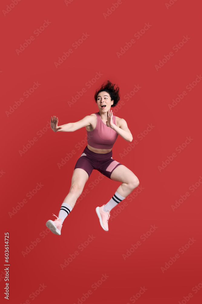 Full length portrait young athletic woman performing a martial arts kick, isolated on red background Full length portrait young athletic woman performing a martial arts kick, isolated on red background