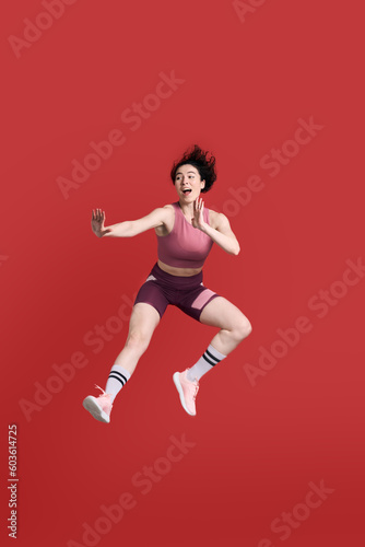 Full length portrait young athletic woman performing a martial arts kick, isolated on red background