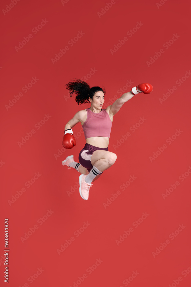 Full size portrait sports woman boxer wearing red boxing gloves, making direct hit, jumping high up Full size portrait sports woman boxer wearing red boxing gloves, making direct hit, jumping high up