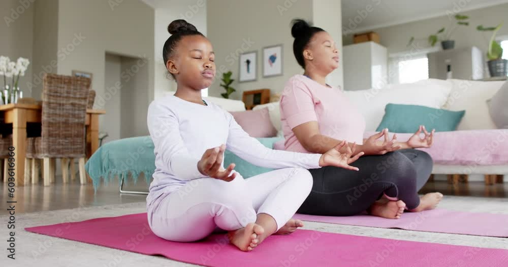 Happy unaltered african american mother and daughter doing yoga meditation at home, in slow motion Happy unaltered african american mother and daughter doing yoga meditation at home, in slow motion