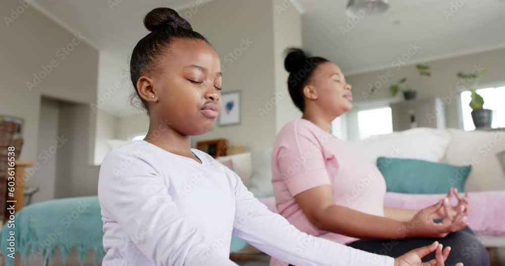 Happy unaltered african american mother and daughter doing yoga meditation at home, in slow motion