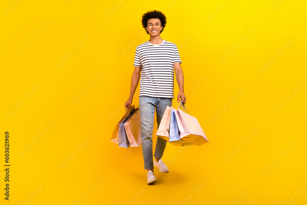 Full length cadre of young shopaholic man black friday advert promo walks hold packages outlet store isolated on yellow color background