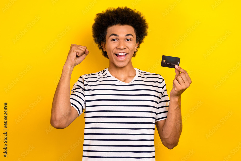 Portrait photo of youngster crazy triumphant businessman fist up hold credit card eshopping advantage isolated on yellow color background Portrait photo of youngster crazy triumphant businessman fist up hold credit card eshopping advantage isolated on yellow color background