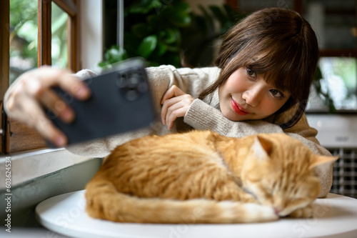 A woman is resting and taking selfies with her chunky, cute orange cat in her living room.