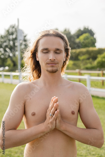 shirtless man with long hair and closed eyes showing anjali mudra gesture while meditating outdoors © LIGHTFIELD STUDIOS