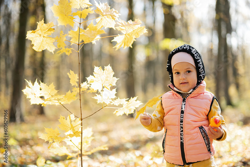 Autumn outdoor portrait of beautiful happy baby girl in forest with woodpecker toy in hands, against yellow leaves.