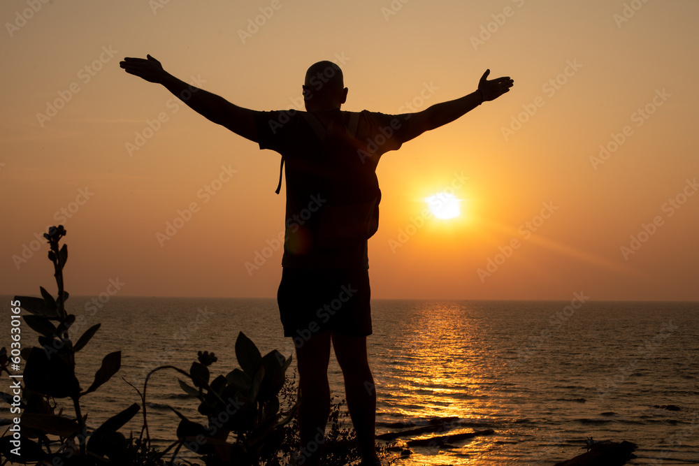 Fototapeta premium Man stand with arms wide open on beach and look at water. Traveler spend past day close to waves, watch sunset.
