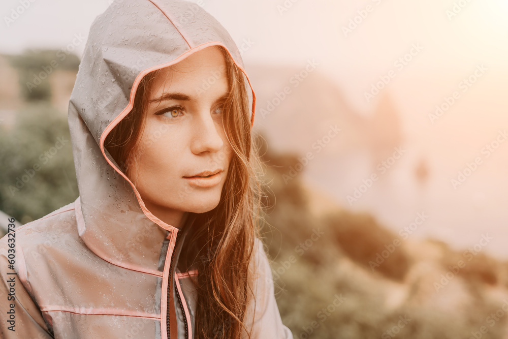 Fototapeta premium Woman rain umbrella. Happy woman portrait wearing a raincoat with transparent umbrella outdoors on rainy day in park near sea. Girl on the nature on rainy overcast day.