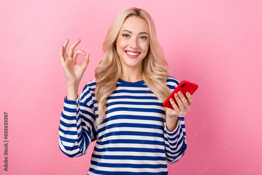 Photo of nice cheerful woman with curly hairdo dressed striped shirt show okey good job hold smartphone isolated on pink color background Photo of nice cheerful woman with curly hairdo dressed striped shirt show okey good job hold smartphone isolated on pink color background