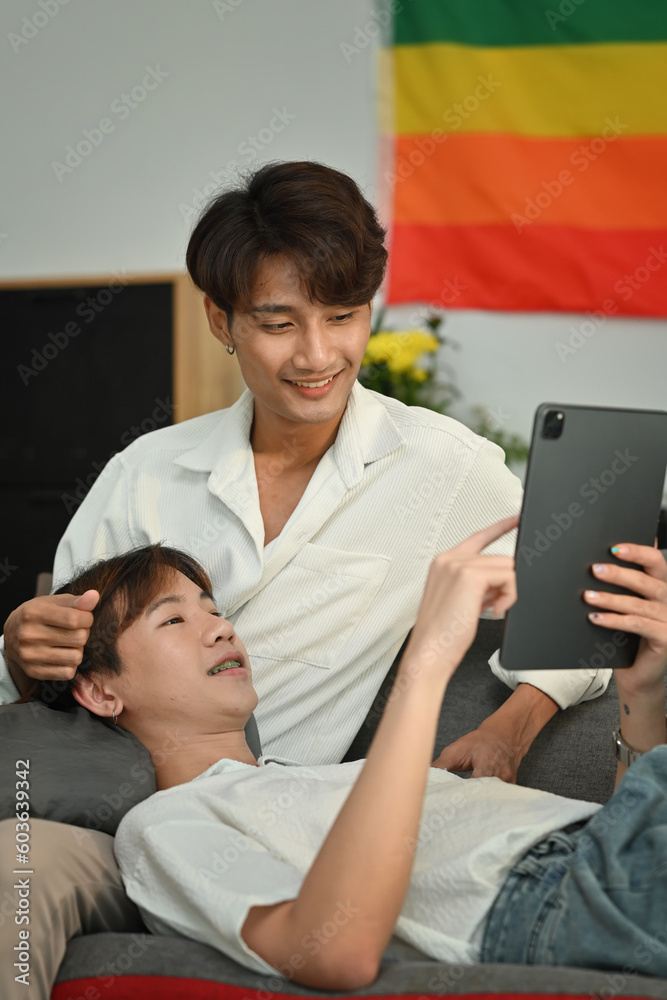 Loving homosexual couple embracing and using digital tablet on couch. LGBT, love and lifestyle relationship concept