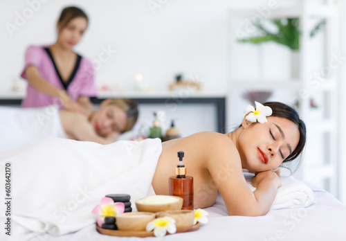 Portrait shot of Millennial Asian young beautiful relaxing resting nude naked woman laying lying down smiling look at camera on comfortable massage bed under clean white towel waiting for masseuse