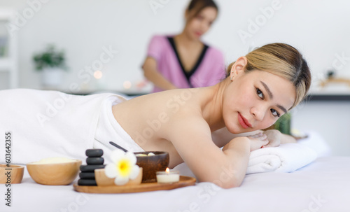 Portrait shot of Millennial Asian young beautiful relaxing resting nude naked woman laying lying down smiling look at camera on comfortable massage bed under clean white towel waiting for masseuse