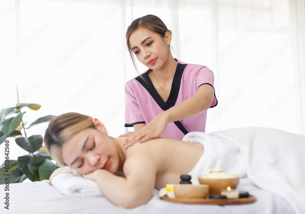 Portrait shot of Millennial Asian young beautiful relaxing resting nude naked woman laying lying down smiling look at camera on comfortable bed while female masseuse massaging shoulder and back Portrait shot of Millennial Asian young beautiful relaxing resting nude naked woman laying lying down smiling look at camera on comfortable bed while female masseuse massaging shoulder and back