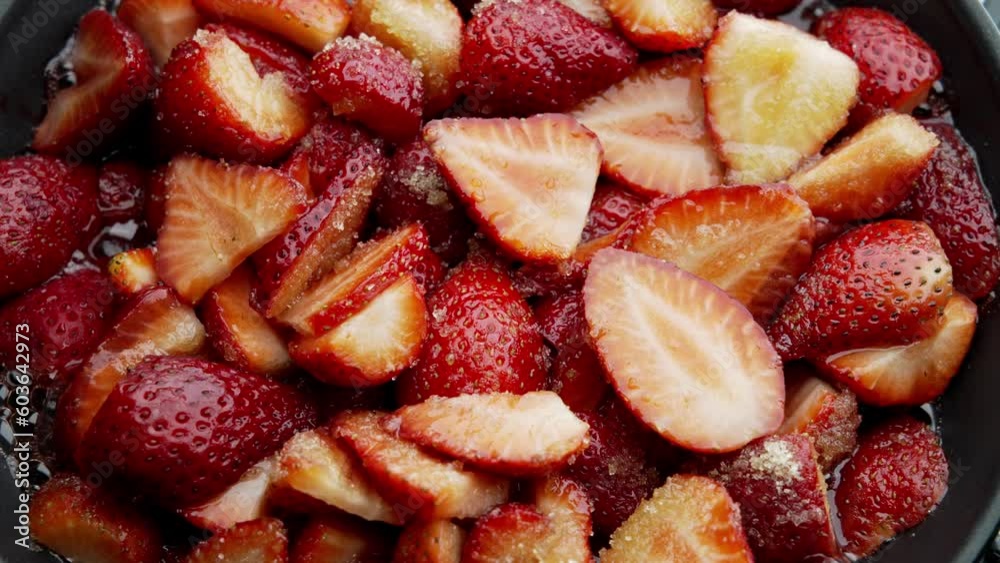 Process of making strawberry jam in its own juice with the addition of sugar in an open bowl on a gas stove macro video shooting