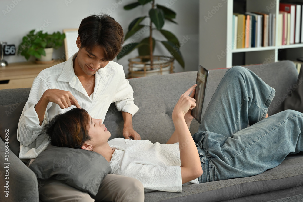 Loving homosexual couple embracing and using digital tablet on couch. LGBT, love and lifestyle relationship concept Loving homosexual couple embracing and using digital tablet on couch. LGBT, love and lifestyle relationship concept