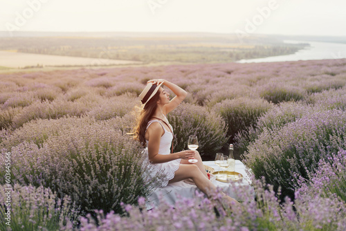 Fototapeta Naklejka Na Ścianę i Meble -  Beautiful woman with in white dress with straw hat having picnic in blooming lavender field.	
